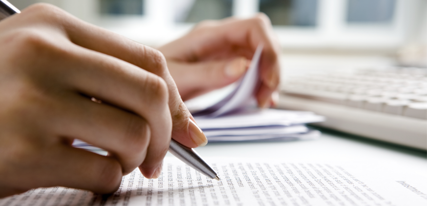 Close up of woman's hand holding a silver pen proofreading a typed document.